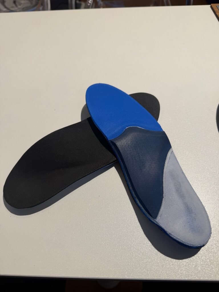 Deux semelles orthopédiques bleues et noires posées sur une table blanche